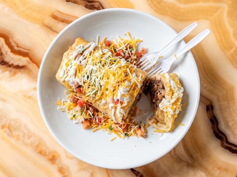 Deep-fried burrito cut in half, topped with cheese, sour cream, and pico de gallo on a white plate.